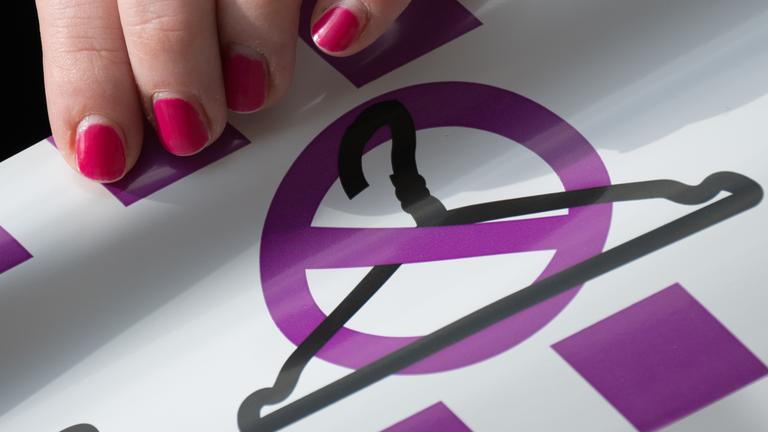 Eine Aktivistin des Bündnisses für sexuelle Selbstbestimmung hält ein Band mit einem durchgestrichenen Kleiderbügel.