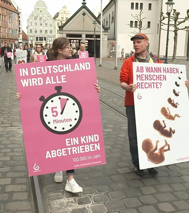 Zwei Demonstranten, links Frau, rechts Mann, mit Plakaten "In Deutschland wird alle 5 Minuten ein Kind abgetrieben" "Ab wann haben Menschen Rechte?"