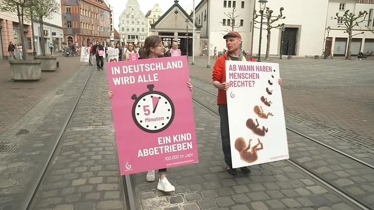 Zwei Demonstranten, links Frau, rechts Mann, mit Plakaten "In Deutschland wird alle 5 Minuten ein Kind abgetrieben" "Ab wann haben Menschen Rechte?"