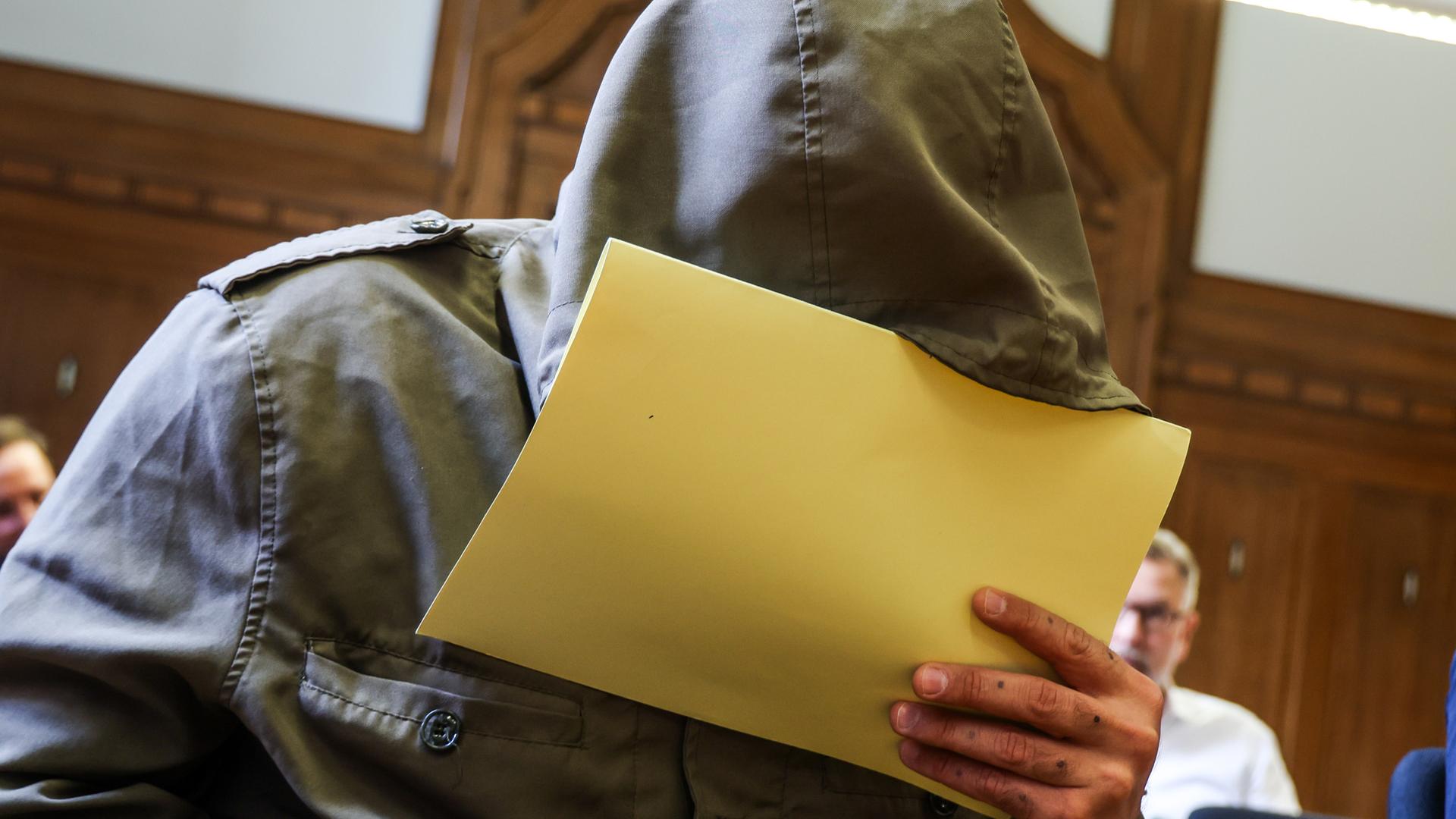 Abu Walaa, früherer IS-Statthalter in Deutschland, sitzt im Gerichtssaal am Verwaltungsgericht in Düsseldorf und hält sich eine Akte vor sein Gesicht.