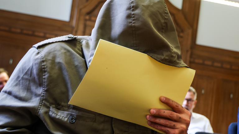 Abu Walaa, früherer IS-Statthalter in Deutschland, sitzt im Gerichtssaal am Verwaltungsgericht in Düsseldorf und hält sich eine Akte vor sein Gesicht.