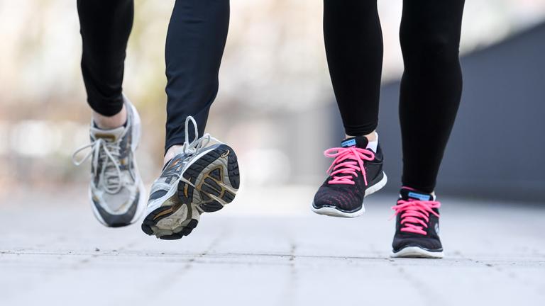 Zu sehen sind die Beine von zwei Personen, die Sportschuhe tragen und joggen.