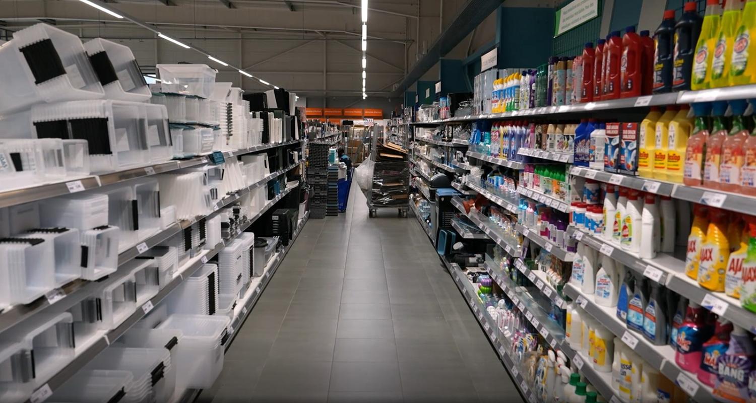 Ein Gang in einem Laden, in den Regalen unterschiedliche Produkte. Rechts stehen Plastikaufbewahrungskisten, links Reinigungsmittel.