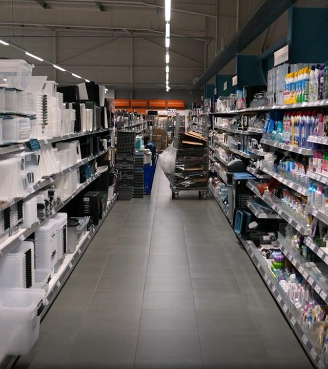Ein Gang in einem Laden, in den Regalen unterschiedliche Produkte. Rechts stehen Plastikaufbewahrungskisten, links Reinigungsmittel.