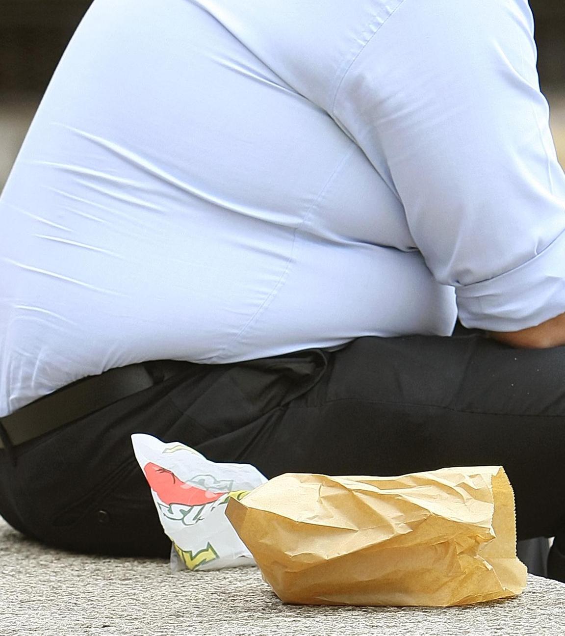 Ein Mann mit starkem Übergewicht sitzt und isst auf dem Bild