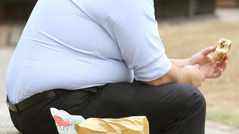 Ein Mann mit starkem Übergewicht sitzt und isst auf dem Bild
