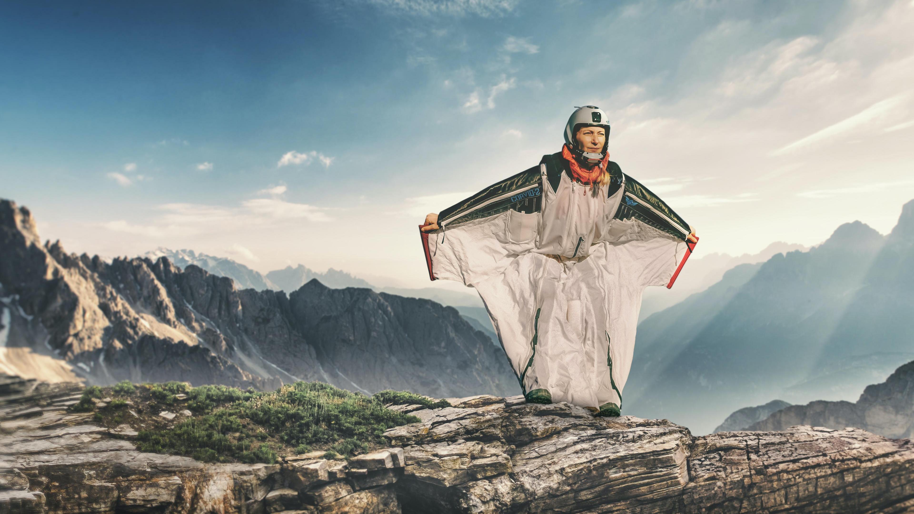 Katja fliegt im Wingsuit in Richtung Kamera. Hinter ihr ragen im Sonnenschein Felswände in den blauen Himmel. 