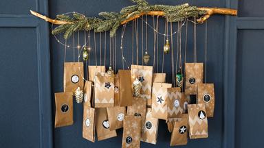 Zu sehen ist ein Adventskalender, bestehend aus Pappumschlägen, die an einem Tannenzweig hängen.