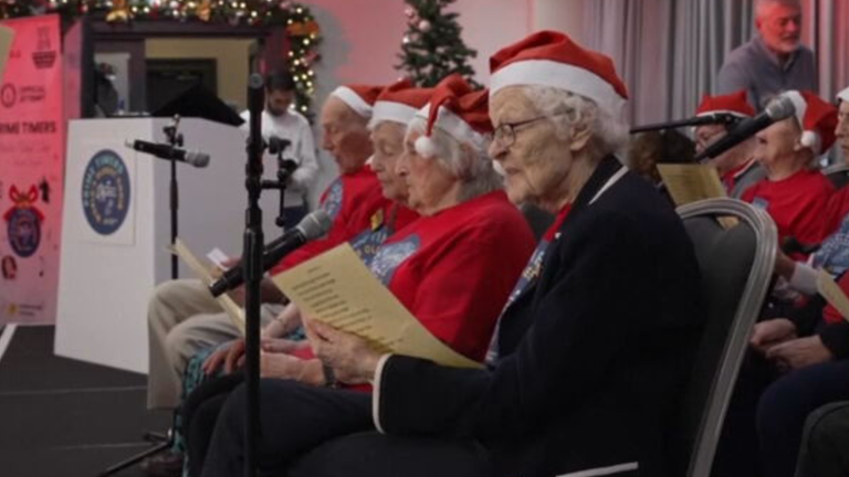 Alte Menschen sitzen mit Weihnachtsmützen auf dem Kopf zusammen und singen Weihnachtslieder.