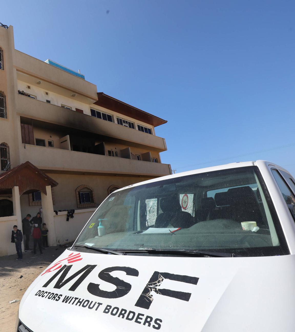 Vor einem dreistöckigen Haus mit einem rußgeschwärzten Balkon steht ein weißer Lieferwagen der Ärzte ohne Grenzen.