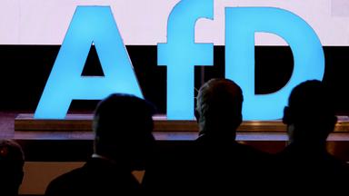 Symbolbild: Delegierte sind beim Landesparteitag der AfD Sachsen vor einem Logo der Partei zu sehen. 