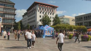 Menschen laufen auf einem Platz, ein Zelt der AfD steht im Hintergrund