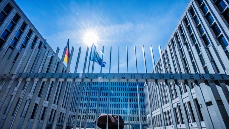 Das Tor des Bundesnachrichtendienstes ist zu sehen und das Gebäude im Hintergrund. Im Hof wehen die Deutschland- und die Europafahne.