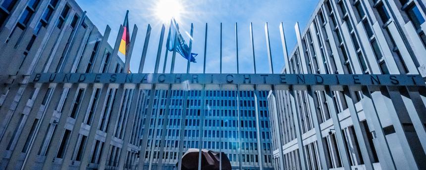 Das Tor des Bundesnachrichtendienstes ist zu sehen und das Gebäude im Hintergrund. Im Hof wehen die Deutschland- und die Europafahne.