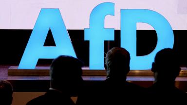 Delegierte sind beim Landesparteitag der AfD Sachsen vor einem Logo der Partei zu sehen