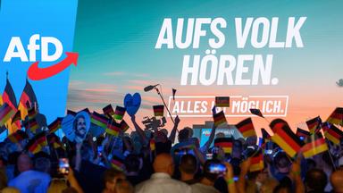 Teilnehmer warten auf den Beginn des Wahlkampfauftakts der AfD Sachsen-Anhalt und schwenken Deutschlandfahnen.