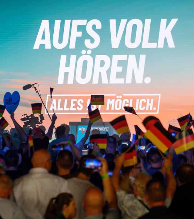 Teilnehmer warten auf den Beginn des Wahlkampfauftakts der AfD Sachsen-Anhalt und schwenken Deutschlandfahnen.