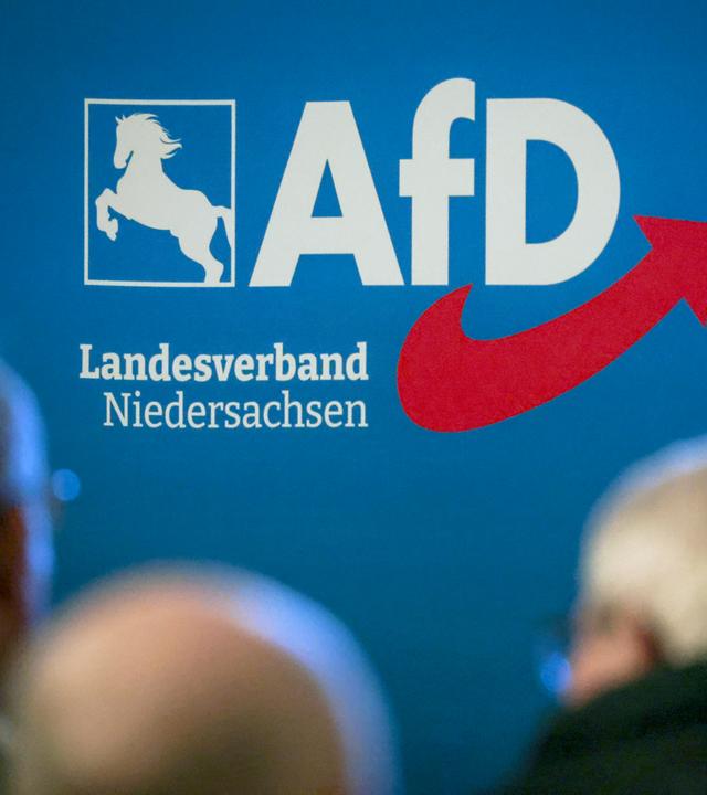 Delegierte sitzen bei der Aufstellungsversammlung der AfD Niedersachsen vor dem Partei-Logo.