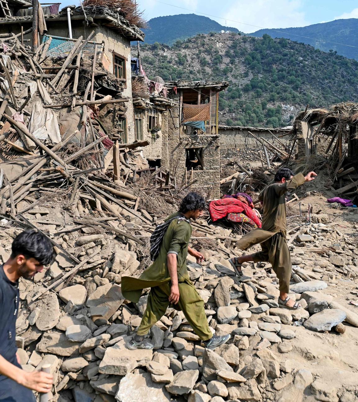 Die Trümmern des Erdbebens in Afghanistan, mit drei Menschen welche durch die Trümmer laufen