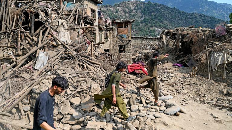 Die Trümmern des Erdbebens in Afghanistan, mit drei Menschen welche durch die Trümmer laufen