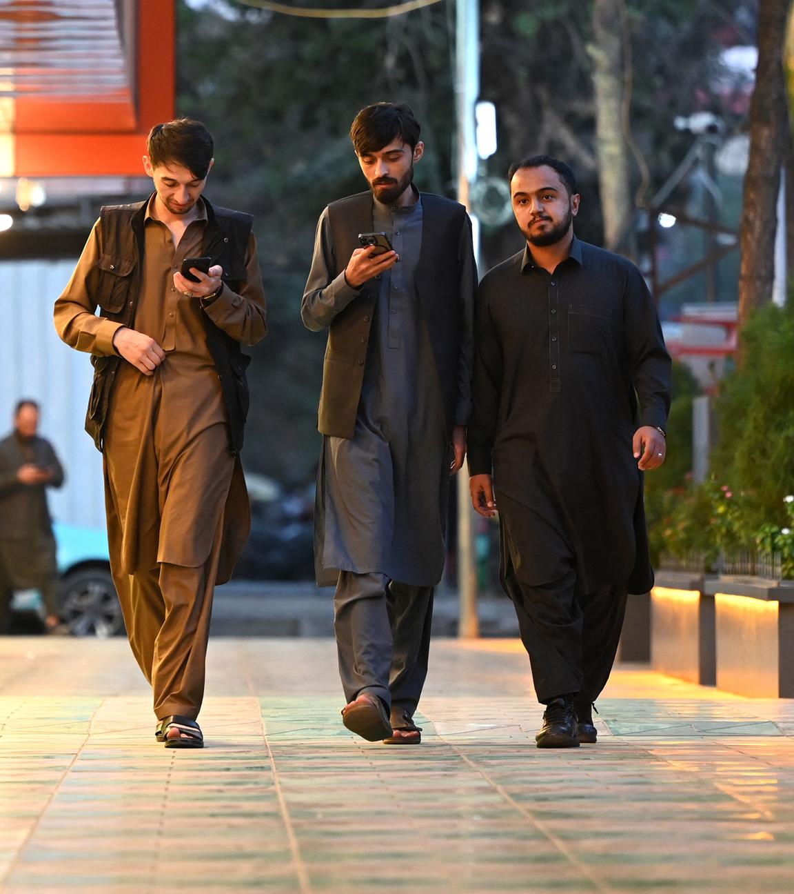 Es sind drei Männer mit Handys in Afghanistan auf der Straße zu sehen.