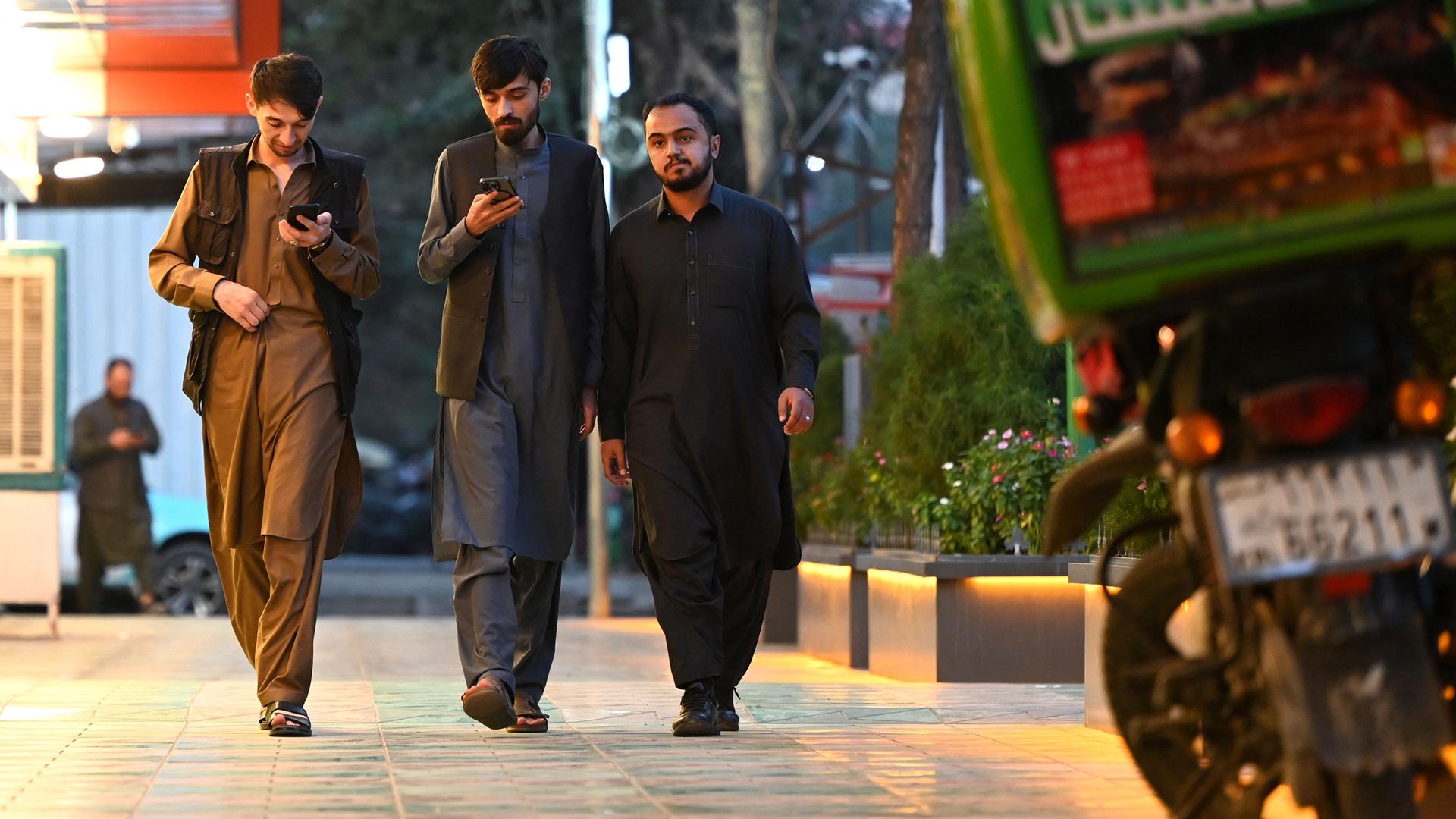 Es sind drei Männer mit Handys in Afghanistan auf der Straße zu sehen.