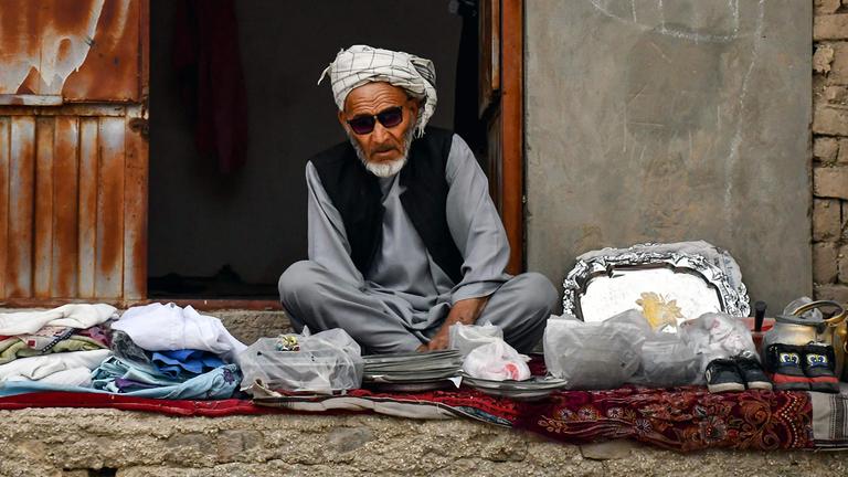 Ein afghanischer Mann, der an der Straße Kleidung verkauft, wartet auf Kunden.