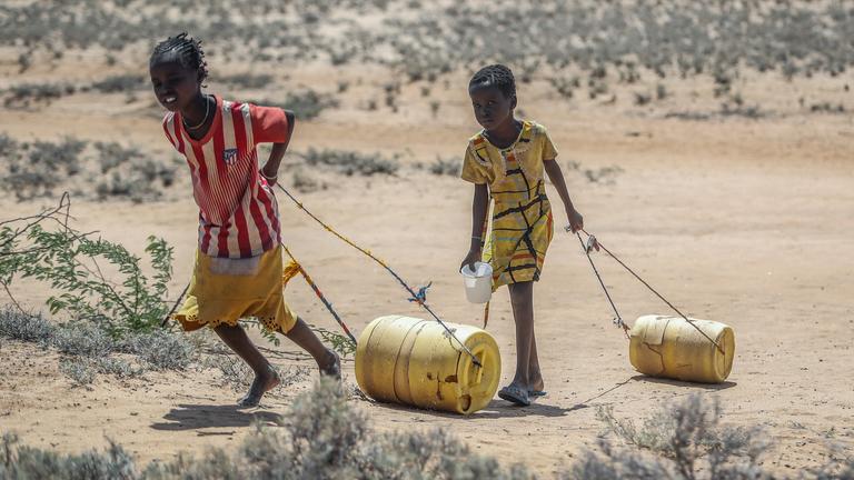 Zwei junge Mädchen ziehen Wasserbehälter auf dem Rückweg zu ihren Hütten in Kenia