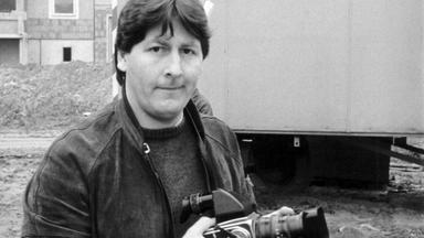 Pierre Boom, Sohne von Günter Guillaume, hält eine Kamara in der Hand. Hinter ihm ist ein Bauwagen sowie eine Häuserzeile.