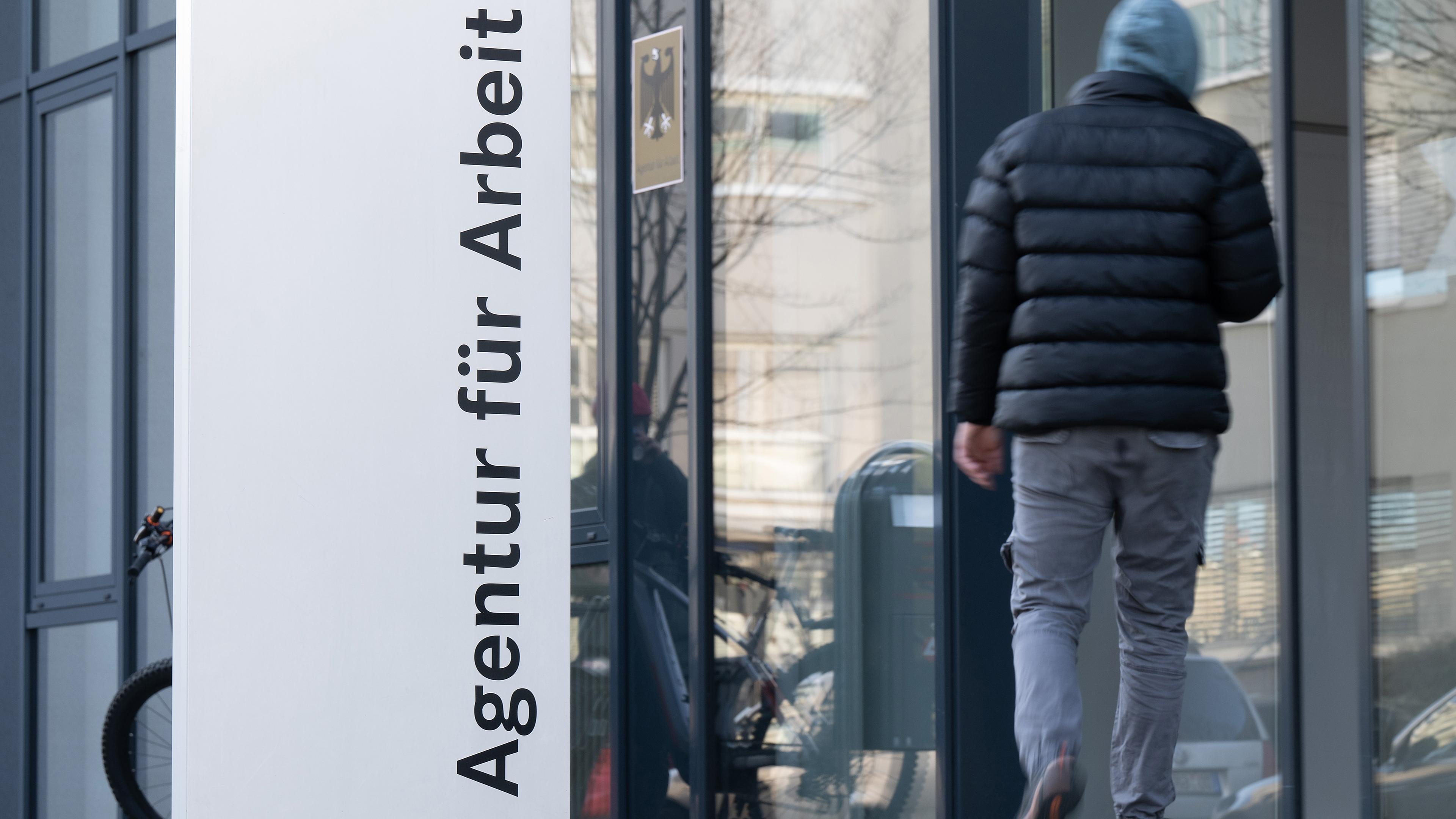 Ein Mann geht hinter einer Stele mit der Aufschrift "Agentur für Arbeit"
