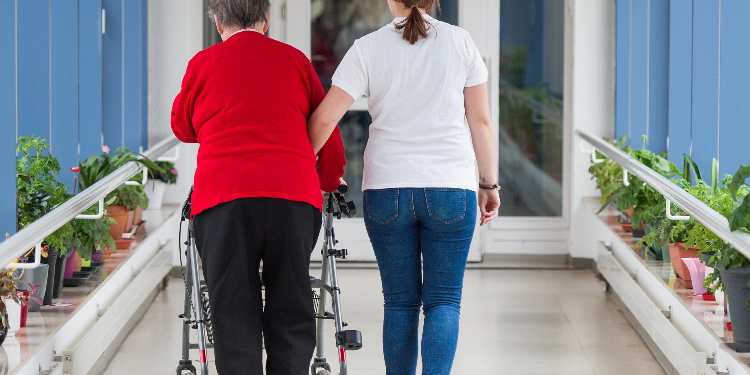 pflegerin fuehrt seniorin mit rollator durch einen flur