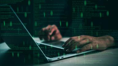 Hände tippen auf einem Laptop mit schwebendem Code, der für Programmierung und Cybersicherheit steht