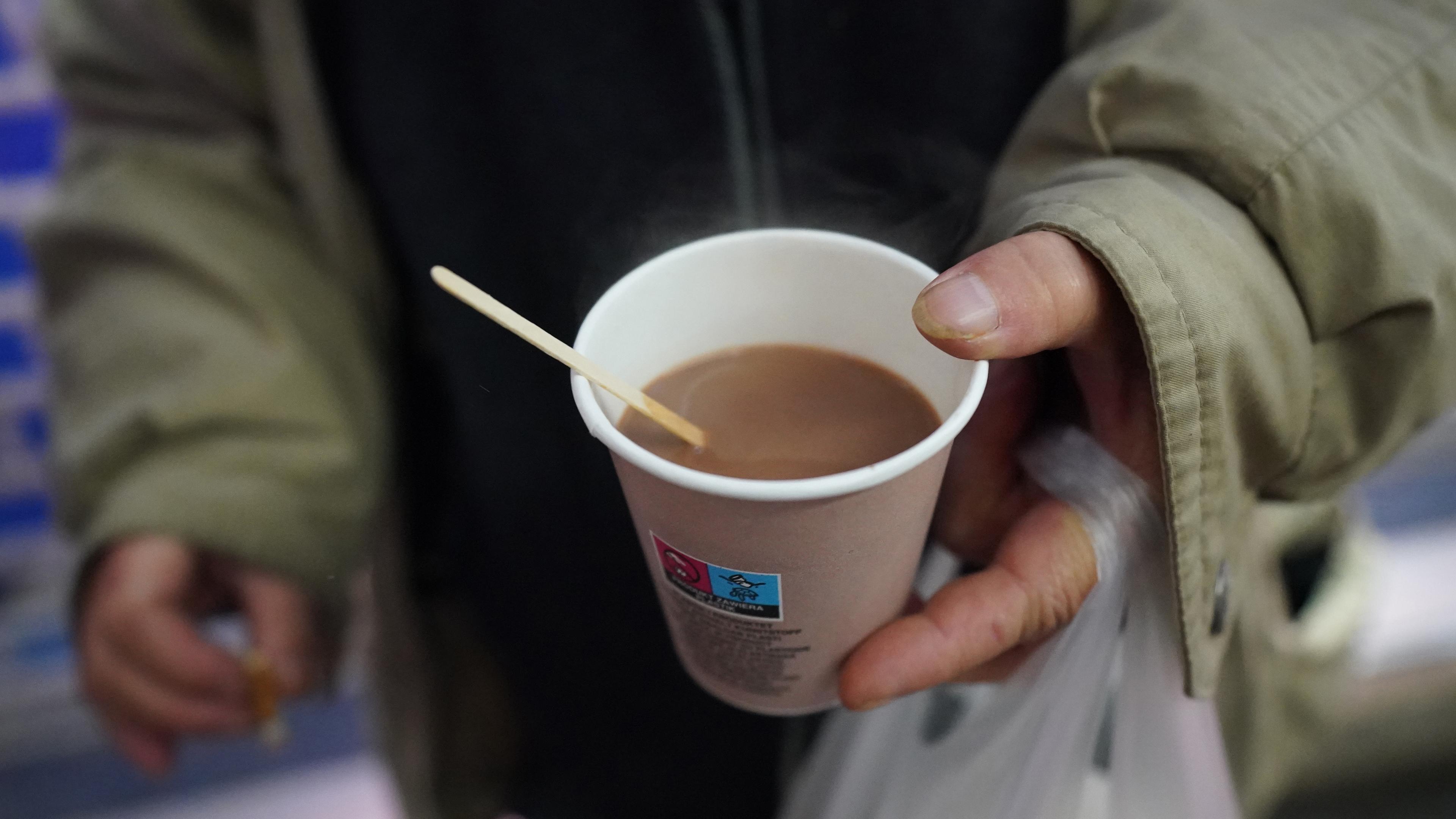 Obdachlose Frau hält einen Kaffee in der Hand