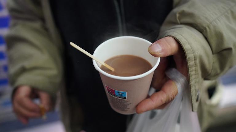 Obdachlose Frau hält einen Kaffee in der Hand