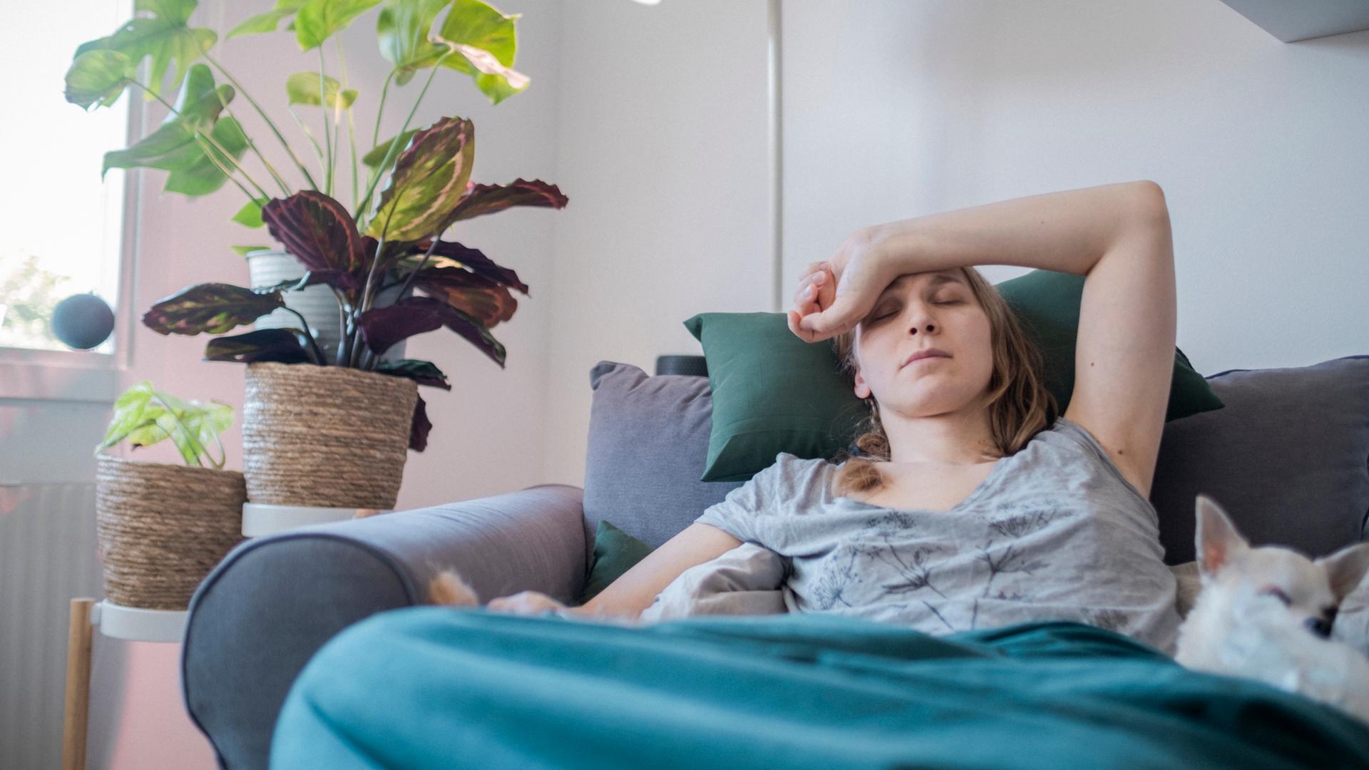 Frau liegt krank zu Hause auf Sofa