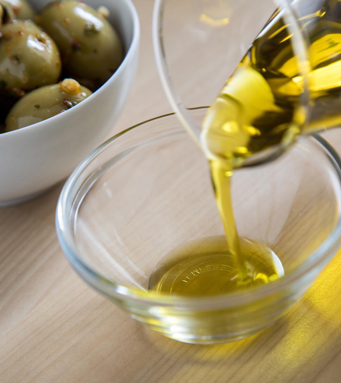 Olivenöl wird aus Karaffe in Glasschale gefüllt