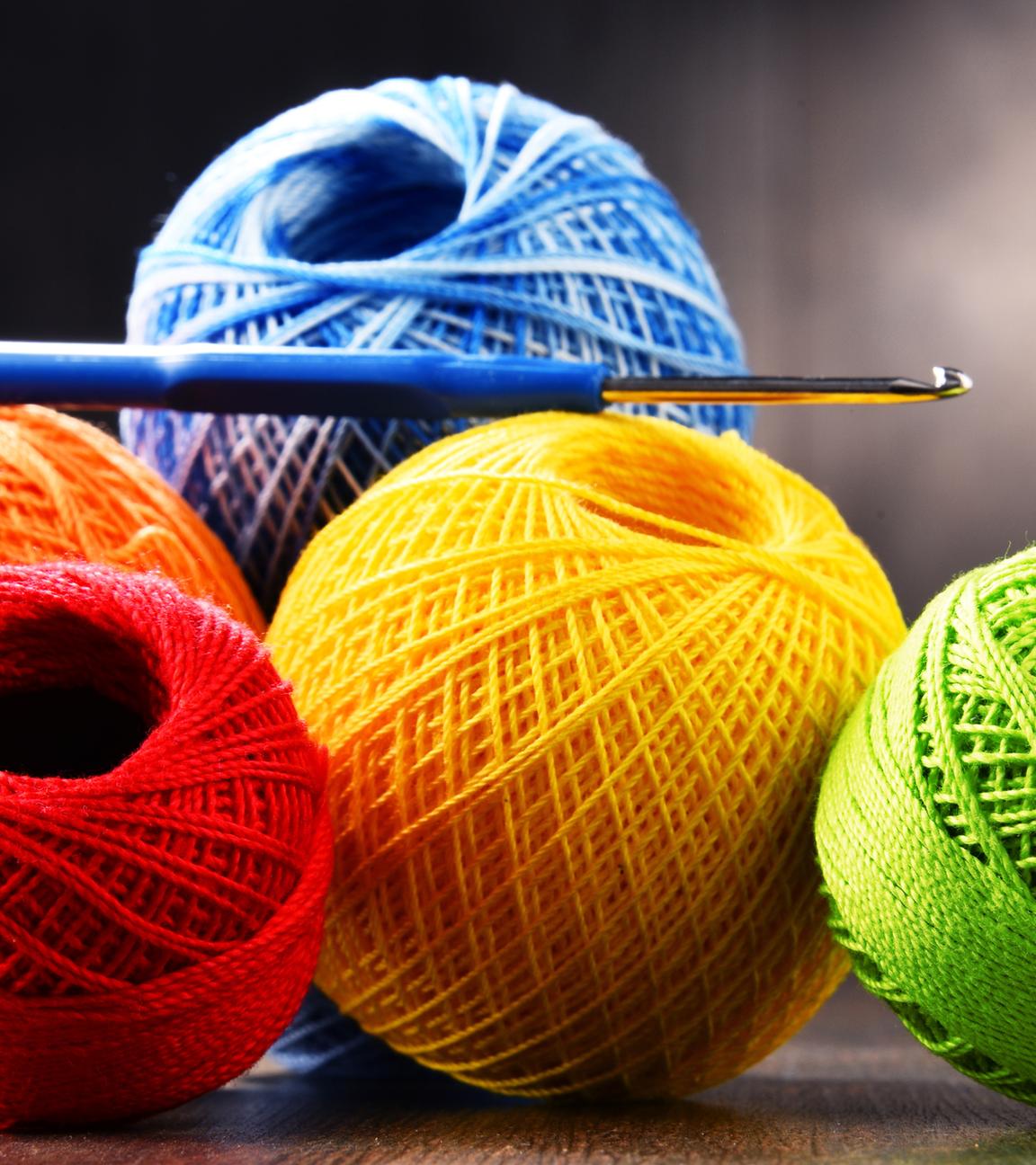 Buntes Garn zum Häkeln und Haken auf einem Holztisch.