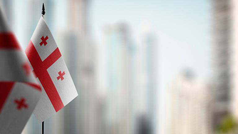 Kleine Flaggen von Georgien auf einem abstrakten unscharfen Hintergrund