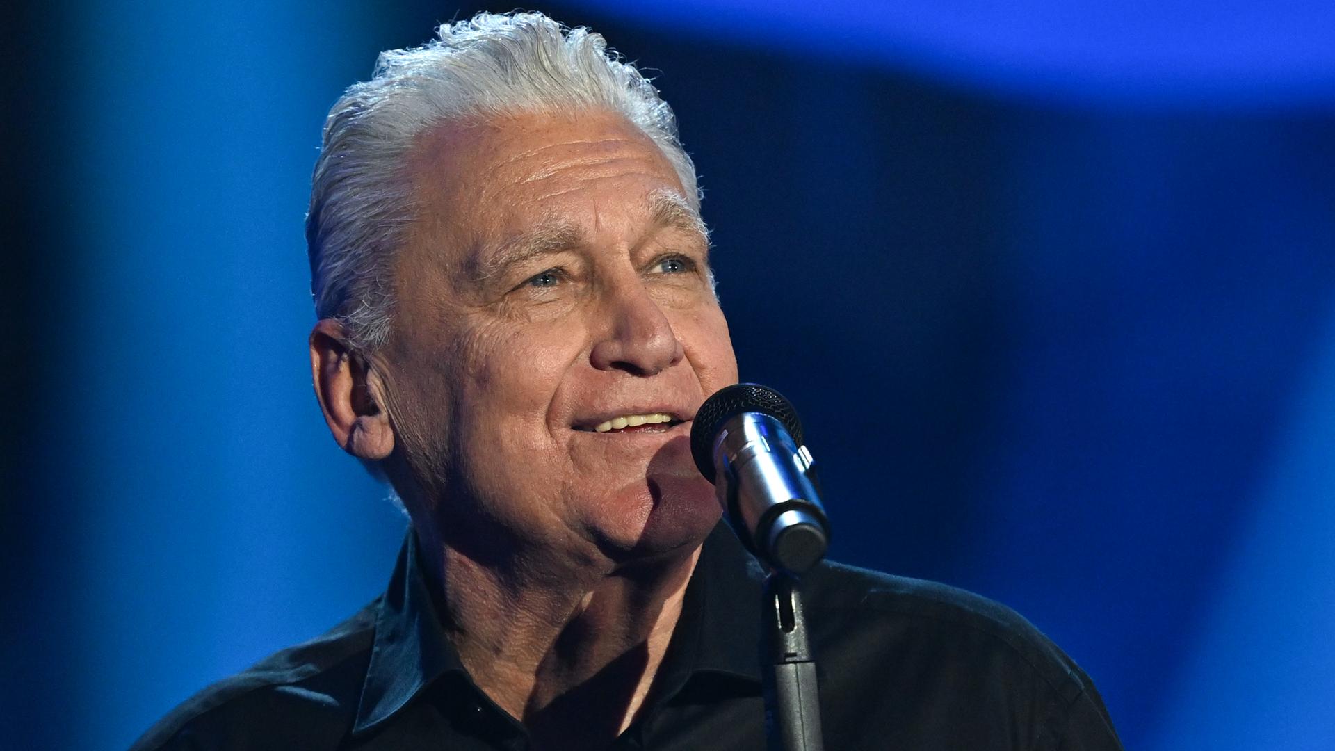 Rainhard Fendrich steht bei einem Auftritt hinter einem Mikrofon.