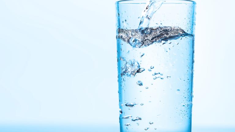 Kristallklares Wasser wird in ein durchsichtiges Glas gegossen und erzeugt erfrischende Wellen und Blasen