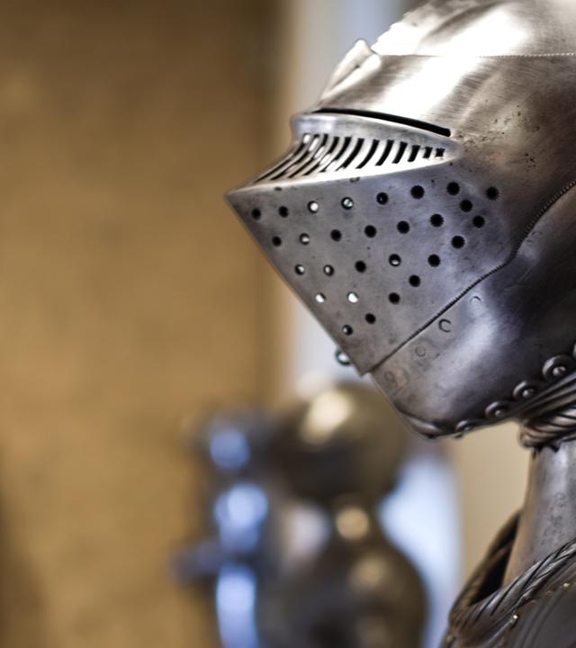 Nahaufnahme des mittelalterlichen glänzenden Helms mit Details und Rüstungen im Hintergrund