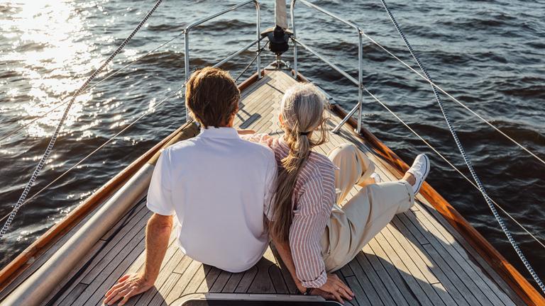 Rearview of two mature people sitting on a yacht bow. Loving senior couple enjoying a boat trip.