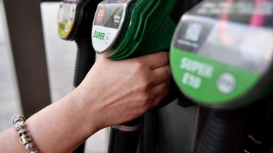 Eine Frauenhand greift nach einer Zapfpistole mit der Aufschrift "Super" an der Tankstelle