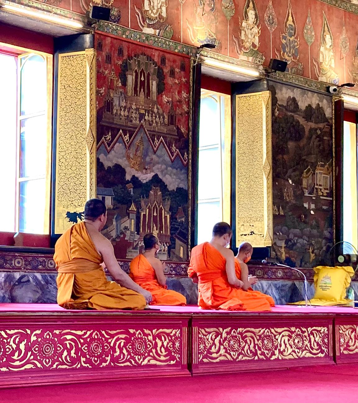 In einem reich geschmückten Tempel sitzen buddhistische Mönche knieend.