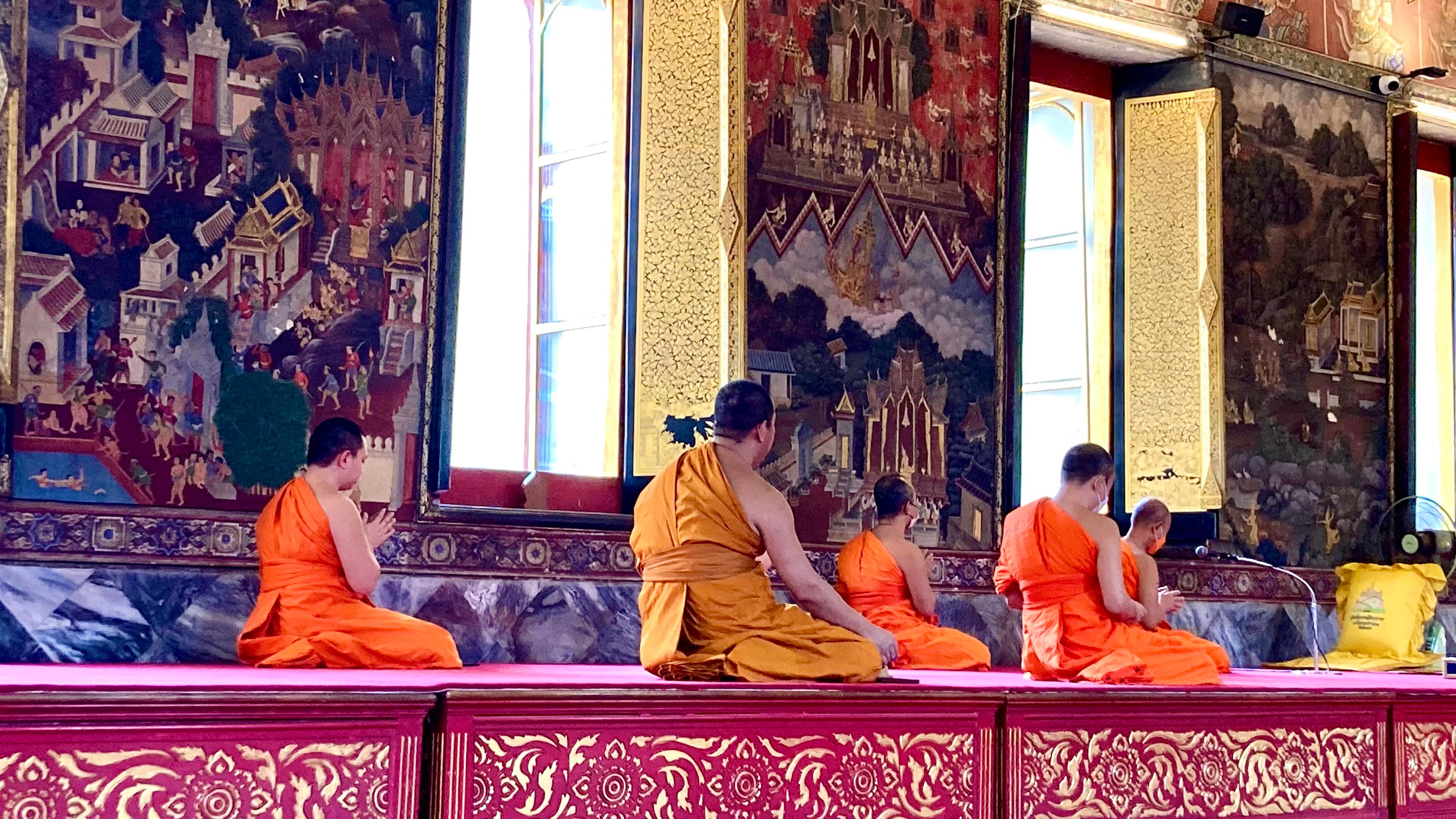 In einem reich geschmückten Tempel sitzen buddhistische Mönche knieend.