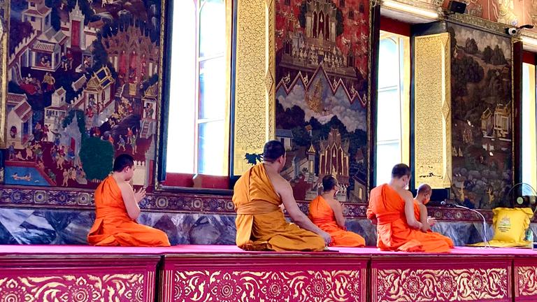 In einem reich geschmückten Tempel sitzen buddhistische Mönche knieend.