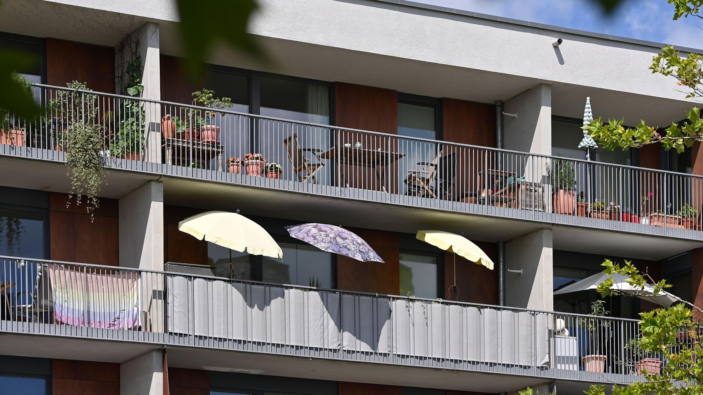 Die Fassade eines Wohngebäudes mit sechs Balkonen, auf dem Balkon in der Mitte sind drei bunte Sonnenschirme aufgeklappt.