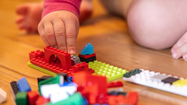 Kind spielt mit bunten Bauklötzen auf Holzboden