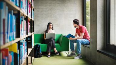zwei StudentInnen unterhalten sich in Bibliothek