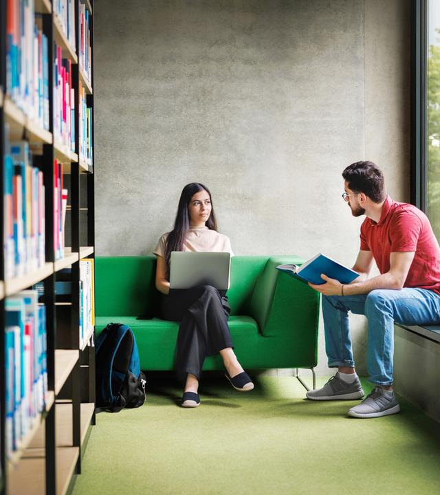 zwei StudentInnen unterhalten sich in Bibliothek